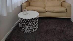 Een woonkamer met een beige bank, een ronde salontafel met een geometrisch ontwerp en een kunstwerk in een lijst aan de muur.
