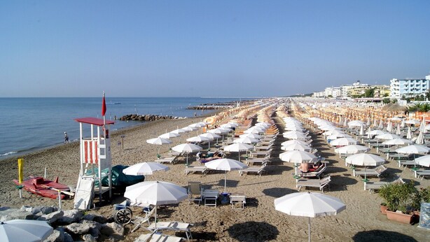 A beach with rows of sunbeds and umbrellas, a lifeguard tower, and a clear view of the sea.