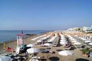 Une plage bordée de rangées de transats et de parasols, une tour de surveillance pour les sauveteurs, et une vue dégagée sur la mer.
