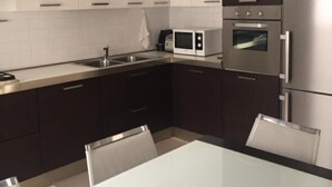 A modern kitchen with white cabinets, a stainless steel refrigerator, a microwave, and a built-in oven.