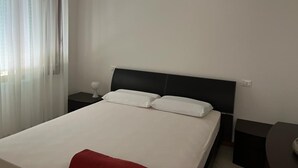 A hotel room with a bed, a bedside table, and a window with sheer curtains.