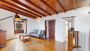 A spacious room with wooden flooring, a sofa, a table, and a staircase.