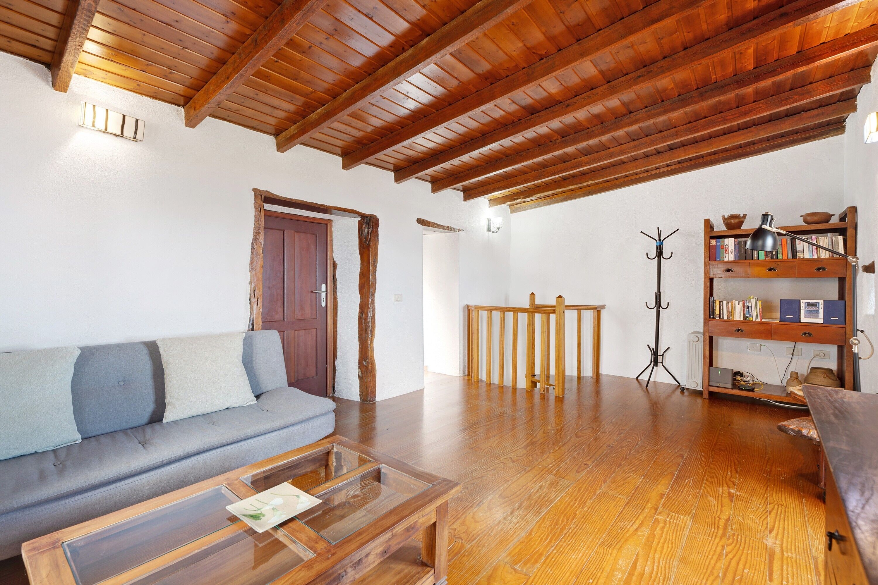 A living room with a wooden ceiling, a sofa, a coffee table, a bookshelf, and a coat rack.