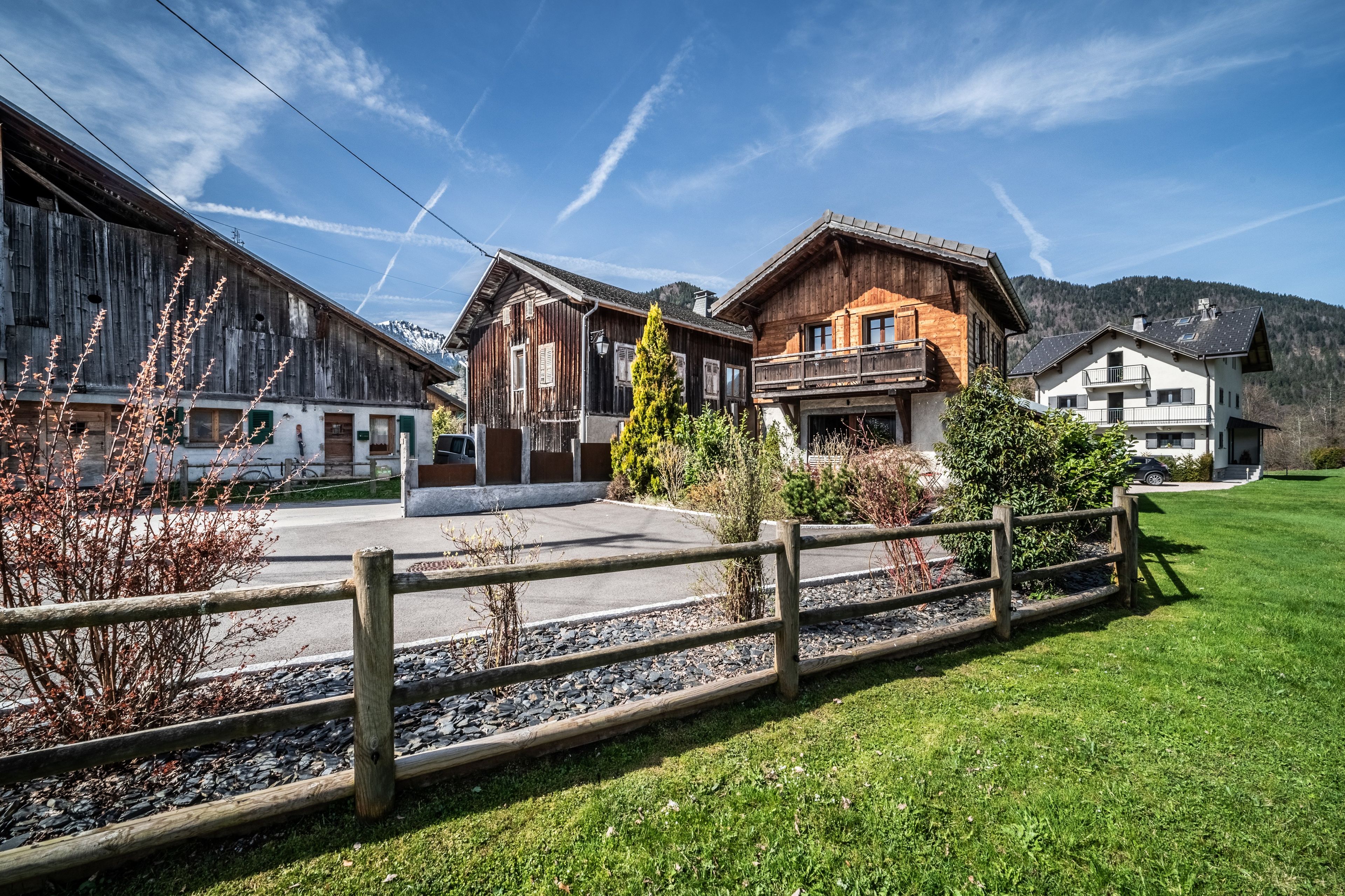 Ein traditionelles Holzhaus mit Balkon, umgeben von einem gepflegten Rasen und einem Holzzaun.