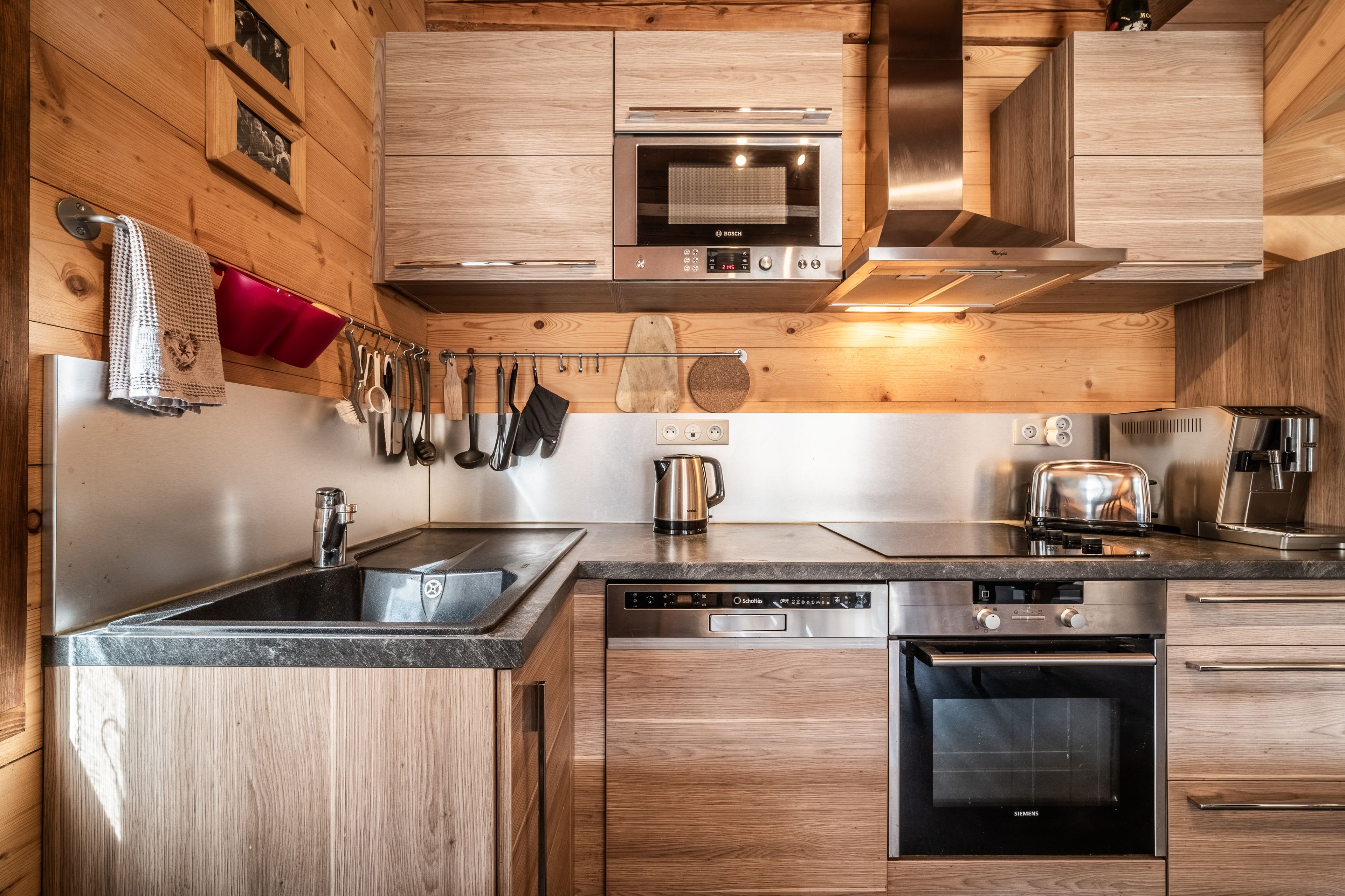 Eine moderne Küche mit Holzschränken, Edelstahlgeräten und verschiedenen Küchenutensilien, die an der Wand hängen.