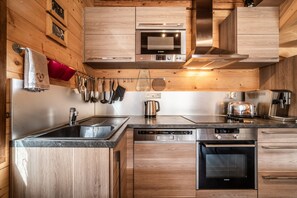 A modern kitchen with wooden cabinetry, stainless steel appliances, and a variety of utensils hanging on the wall.