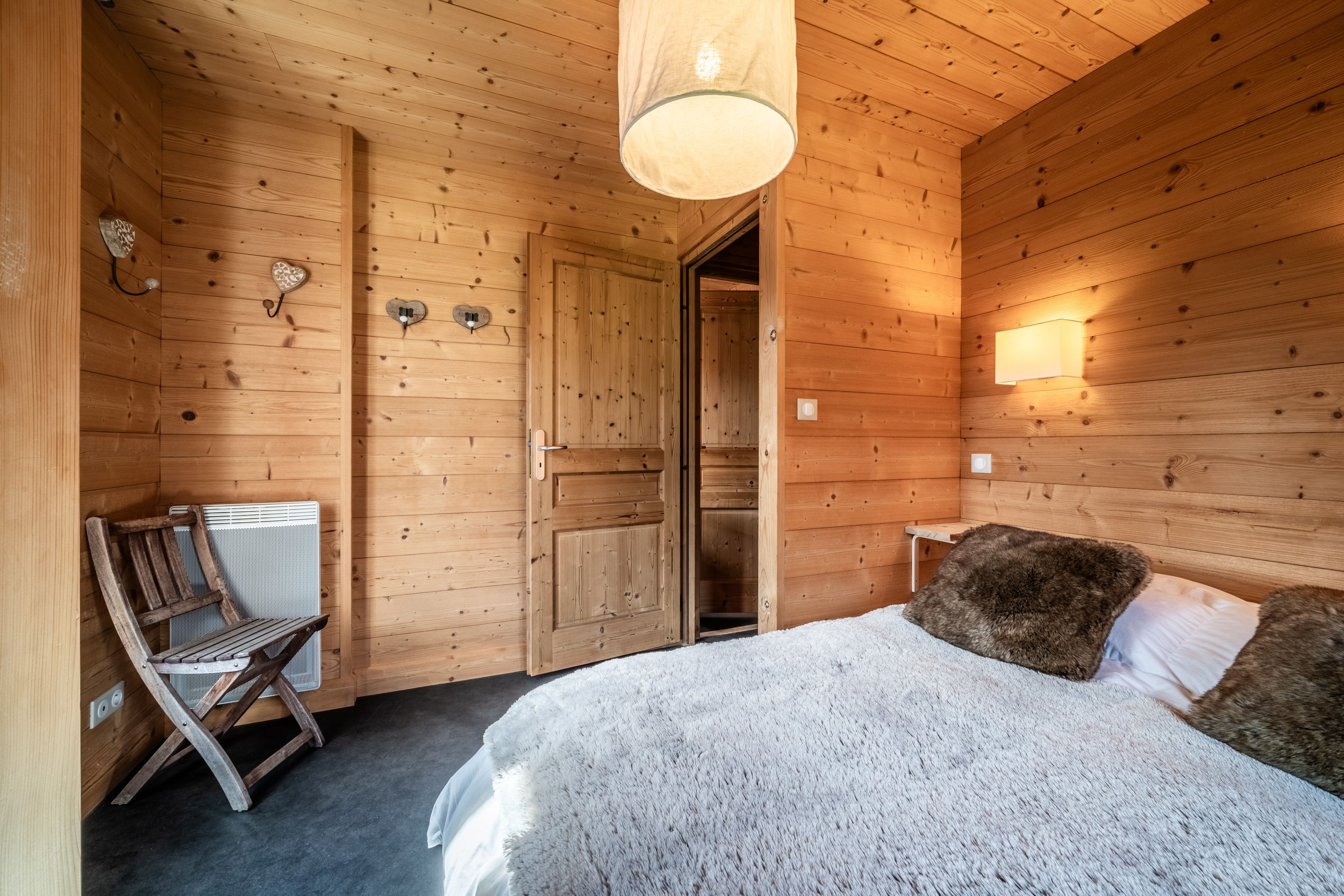 Een houten kamer met een bed, een stoel en een deur.