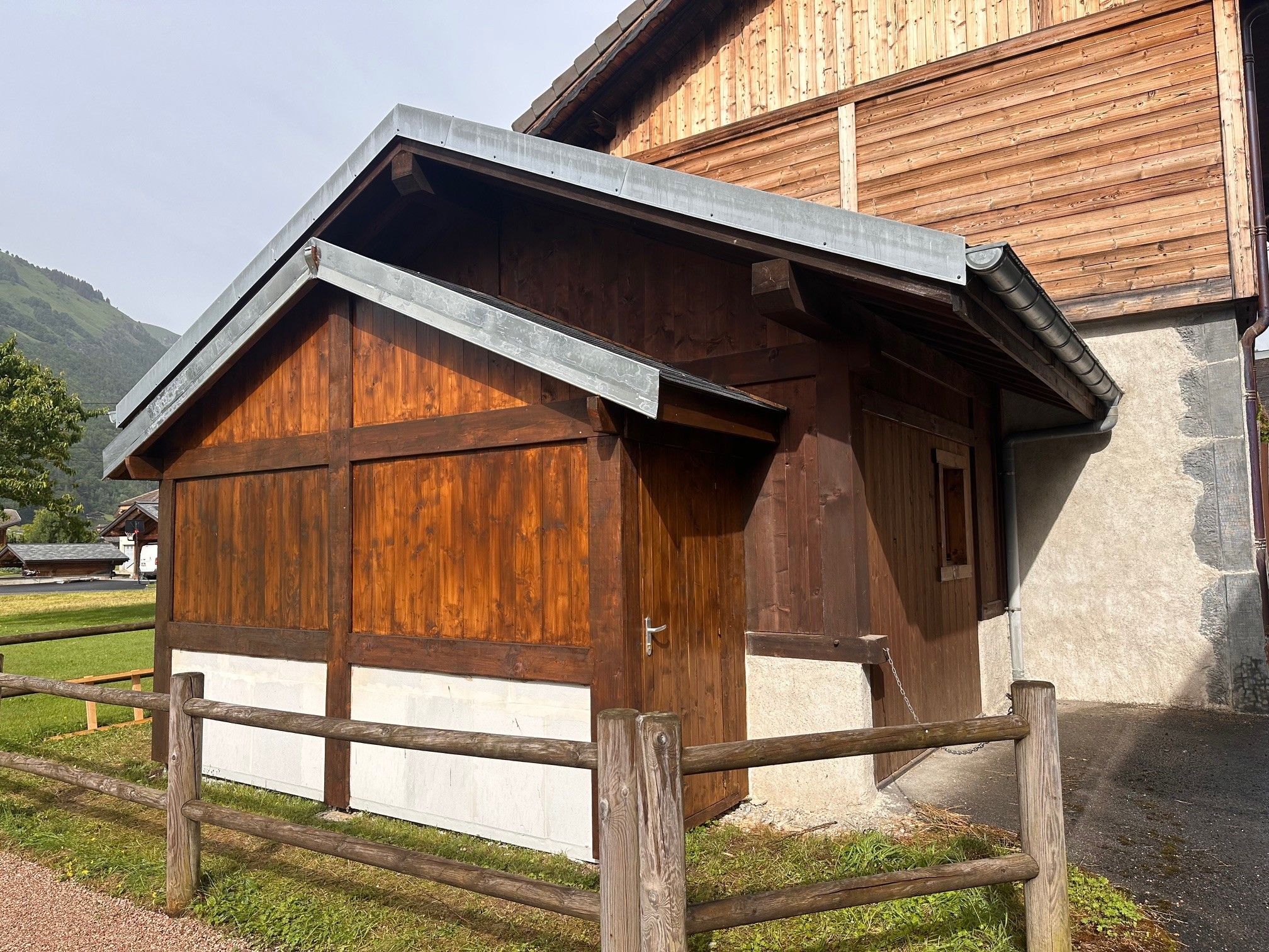 Un bâtiment en bois doté d’un toit en pente, d’une porte et d’une zone délimitée par une clôture.