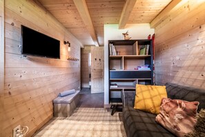 A cozy room with a flat-screen TV mounted on the wall, a wooden bookshelf, a sofa with cushions, and a small bench.