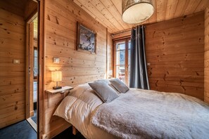 Ein Schlafzimmer einer Holzhütte mit einem Bett, einem Nachttisch, einer Lampe und einem Fenster mit Vorhängen.