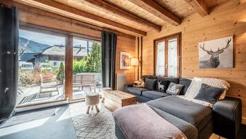 Intérieur moderne d’une cabane en rondins, comprenant un canapé, un lit, un coin repas et une vue sur l’extérieur.