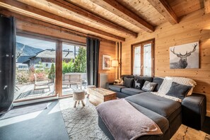 Interior d'una cabana de fusta moderna amb un sofà, un llit, zona de dinar i vista cap a l'exterior.