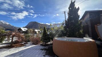 Un espace extérieur enneigé avec un jacuzzi, un bâtiment en bois et des montagnes en arrière-plan.