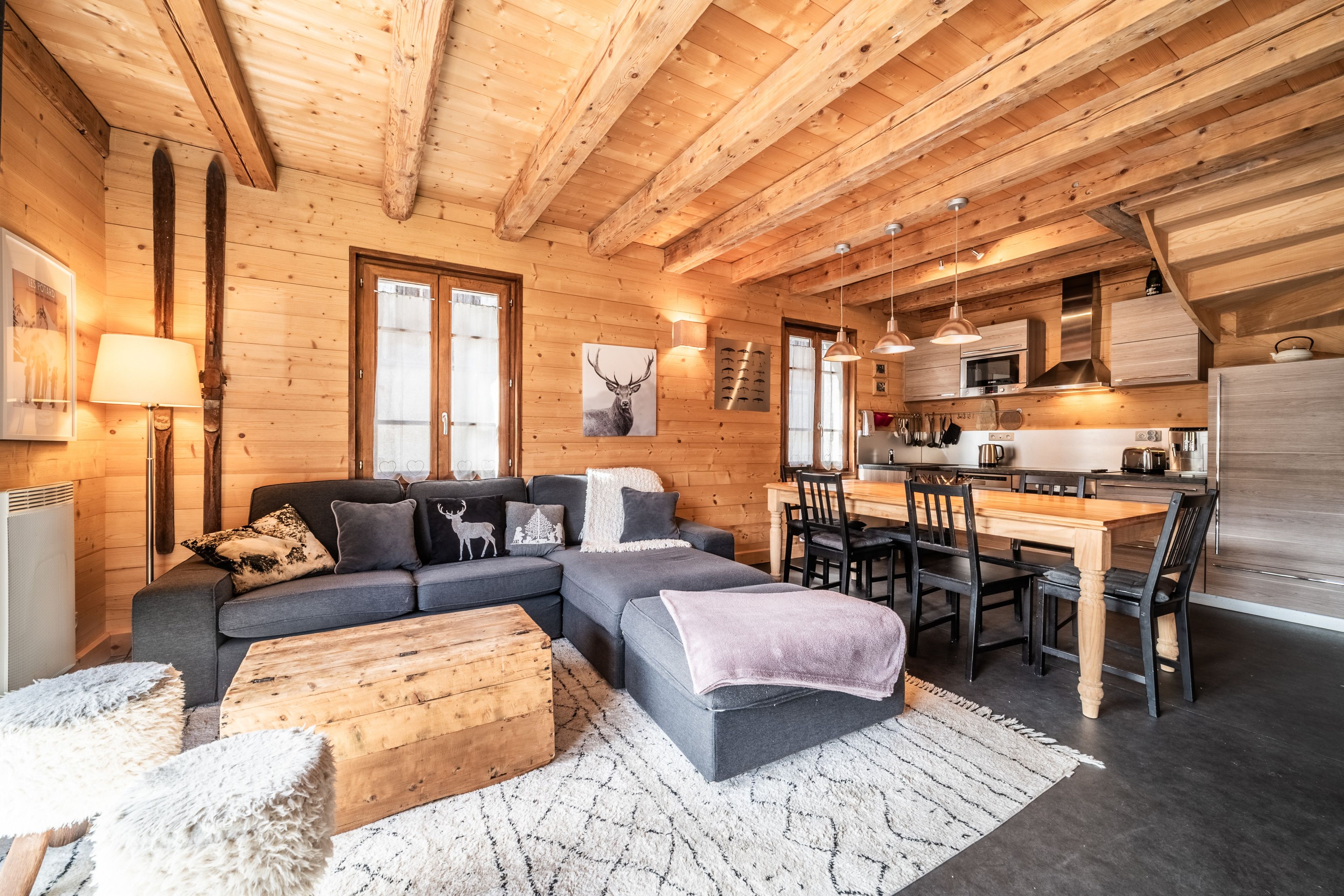 Een gezellig blokhutinterieur met houten plafond, een bank, een eettafel en een keukenhoek.