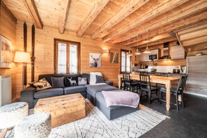 Ein gemütliches Blockhaus-Interieur mit Holzbalkendecke, einer Couch, einem Esstisch und einer Küchenzeile.