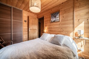 A wooden cabin room with a bed, a wooden wardrobe, and a framed picture on the wall.