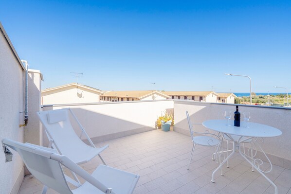 Une terrasse sur le toit avec des chaises longues blanches, une table ronde avec deux verres à vin et une plante en pot.