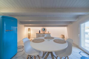 Une cuisine moderne avec un réfrigérateur bleu, des armoires blanches et une table de salle à manger ronde, assortie de chaises blanches.
