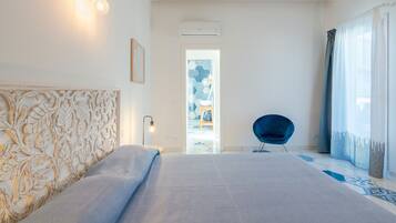 A modern bedroom with a large bed, a decorative headboard, a blue chair, and a view through a doorway.