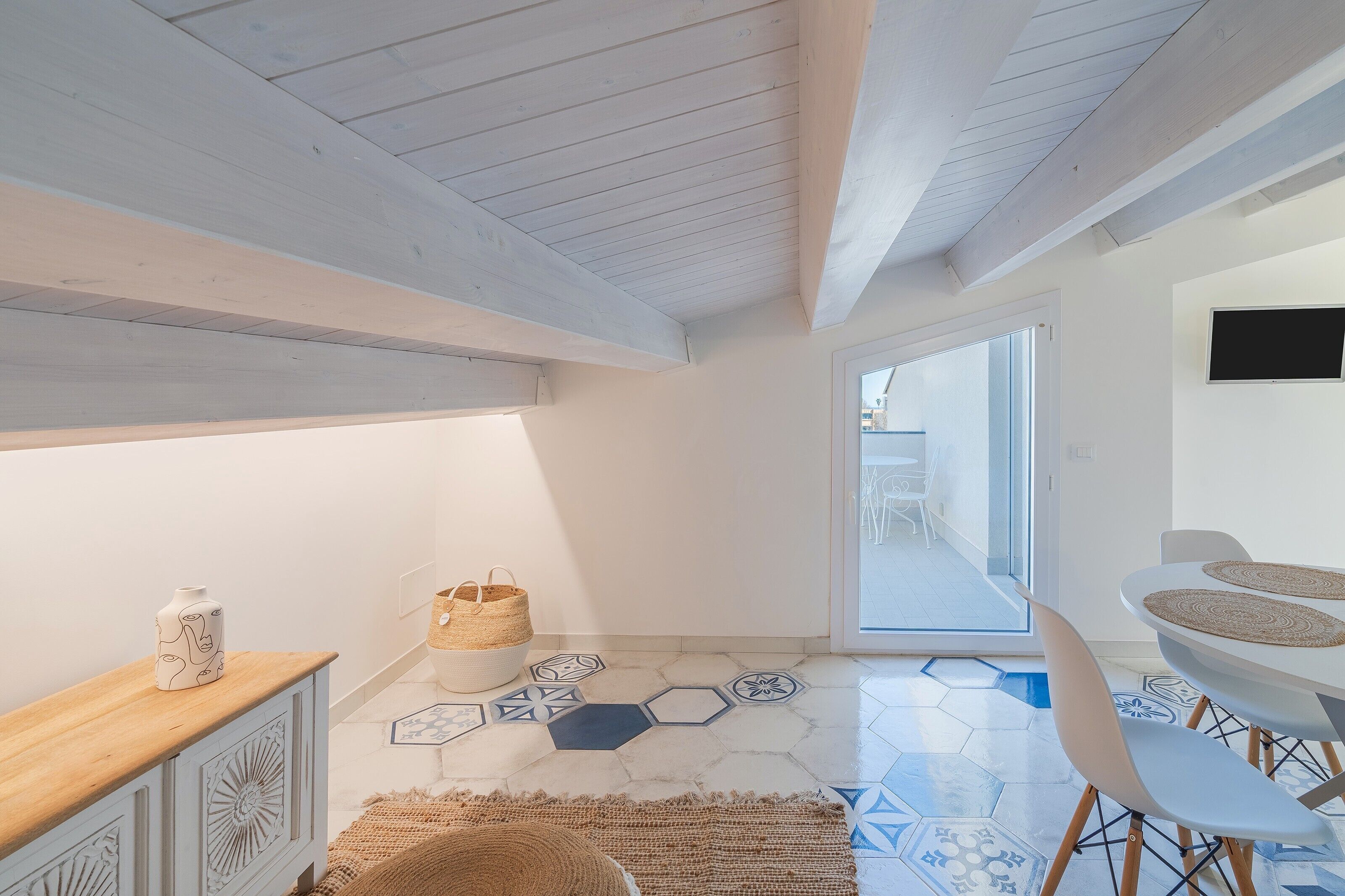 Un intérieur moderne avec un plafond en bois, un coin repas comprenant une table et des chaises, et une vue sur l’extérieur à travers une porte vitrée.