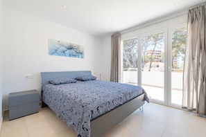 A bedroom with a bed, a nightstand, a window with curtains, and a painting on the wall.