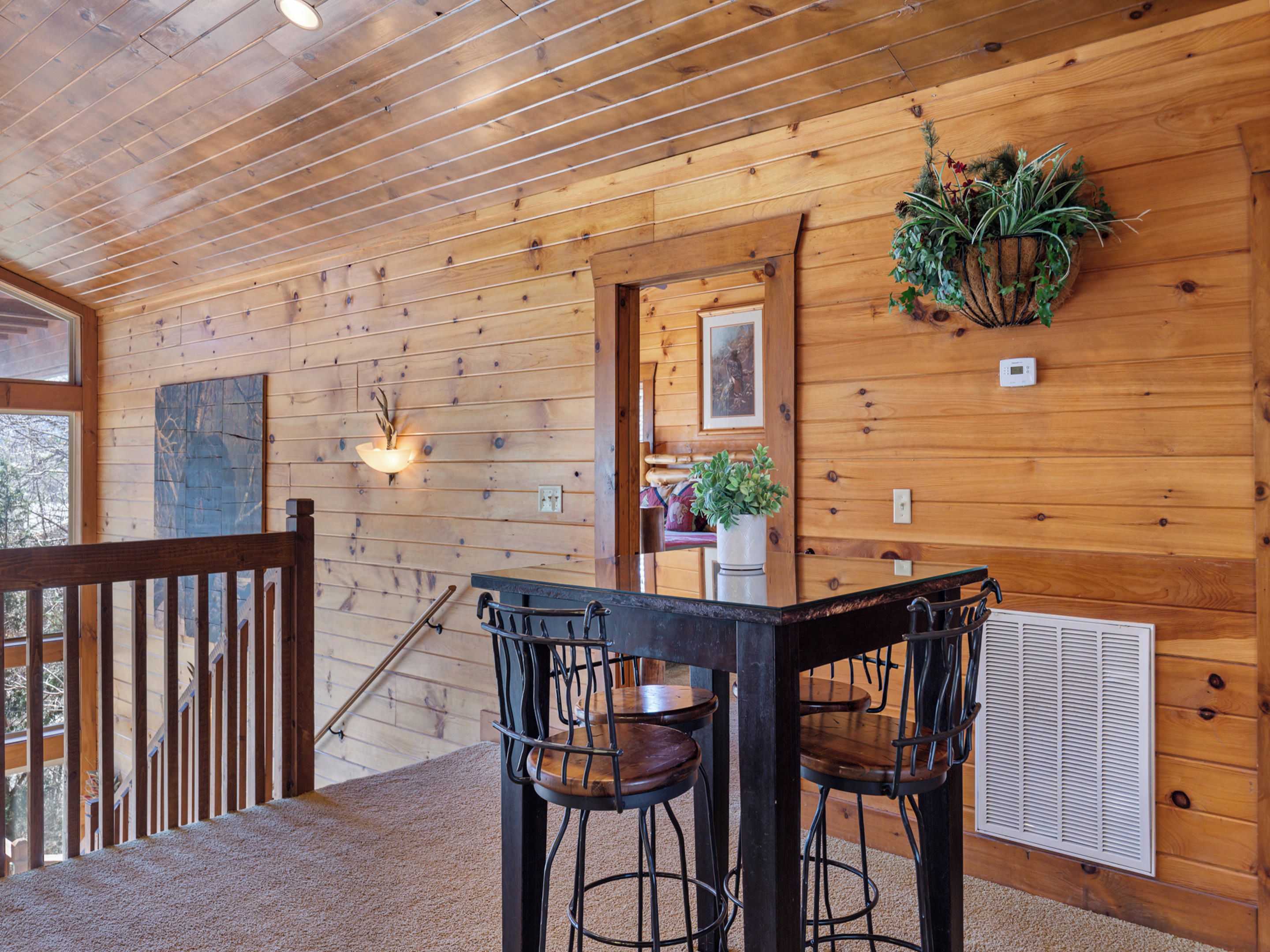 A wooden interior with a wooden table and chairs, a hanging plant, and a framed picture on the wall.