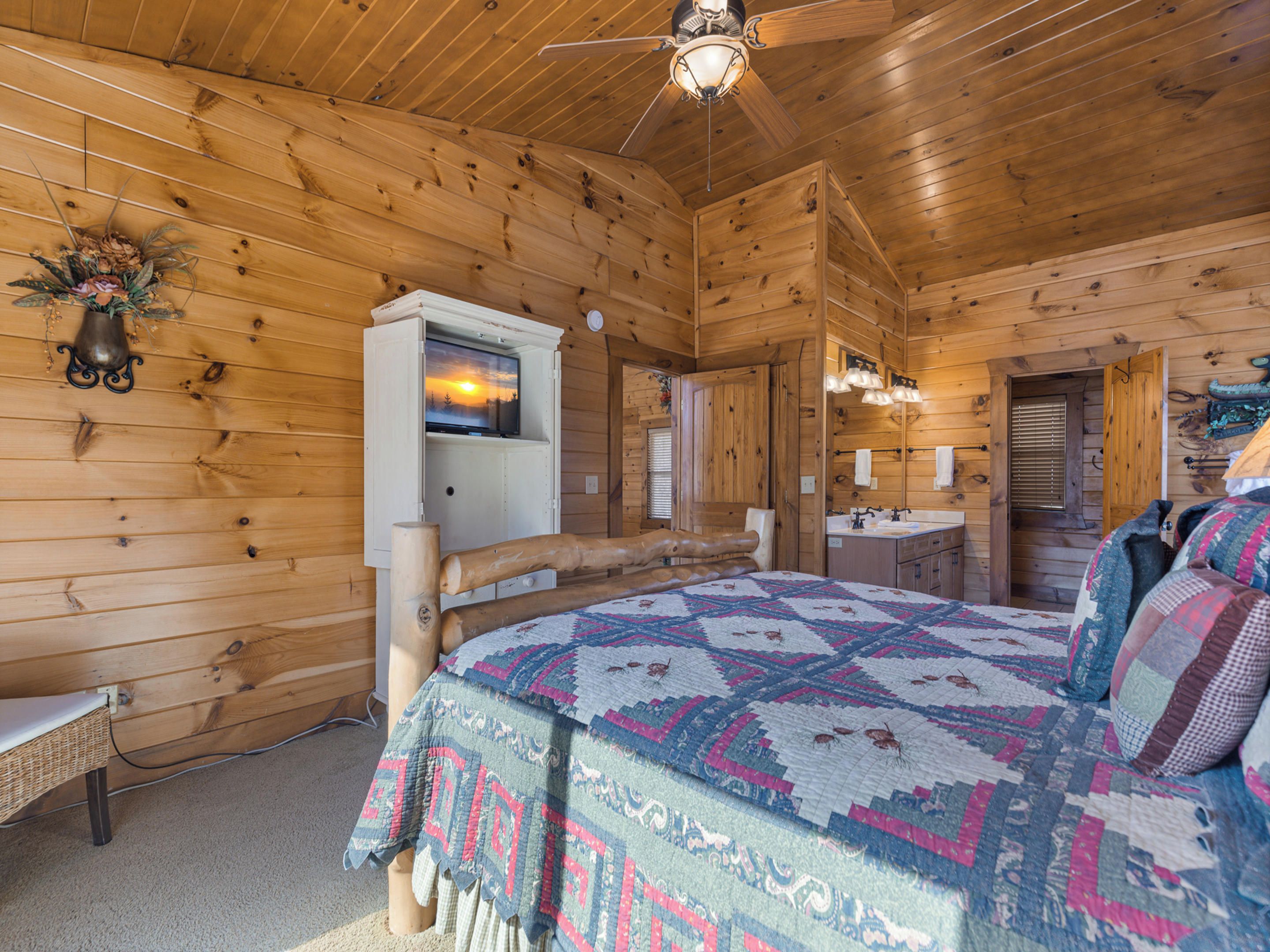 Een slaapkamer in een blokhut met een bed, een kaptafel en een televisie aan de muur.