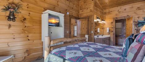 Een slaapkamer in een blokhut met een bed, een kaptafel en een televisie aan de muur.
