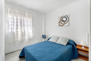 A bedroom with a bed, a bedside table, a lamp, a window with curtains, and a wall art piece.