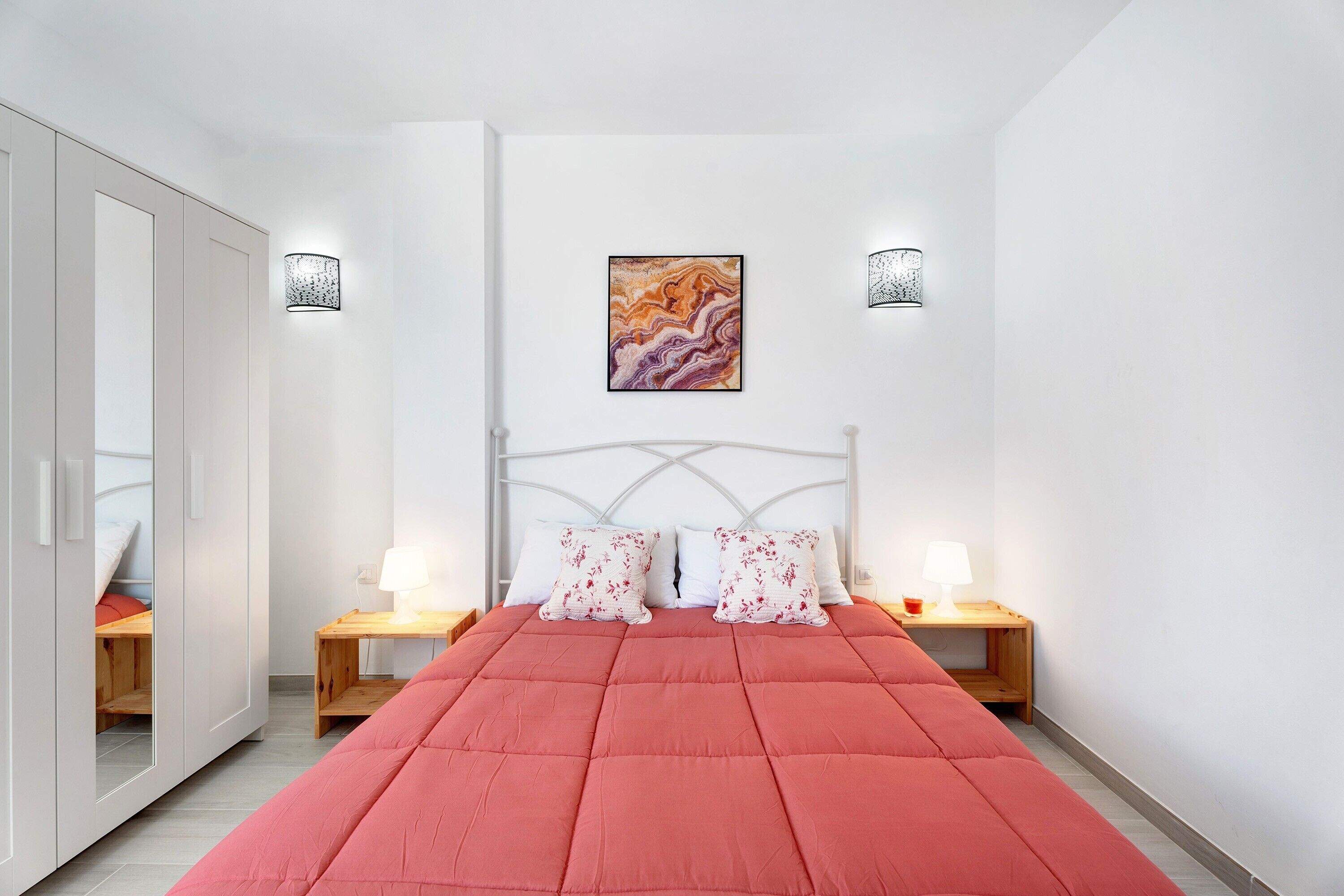 Un dormitorio con una cama, dos mesitas de noche con lámparas, un armario y un cuadro en la pared.