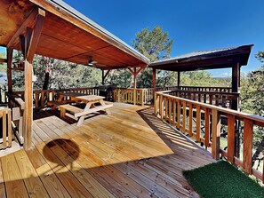 A wooden deck with picnic tables and a ceiling fan, surrounded by a wooden railing. - Enchanted Forest by Ruidoso Vacation Rentals (Alto)