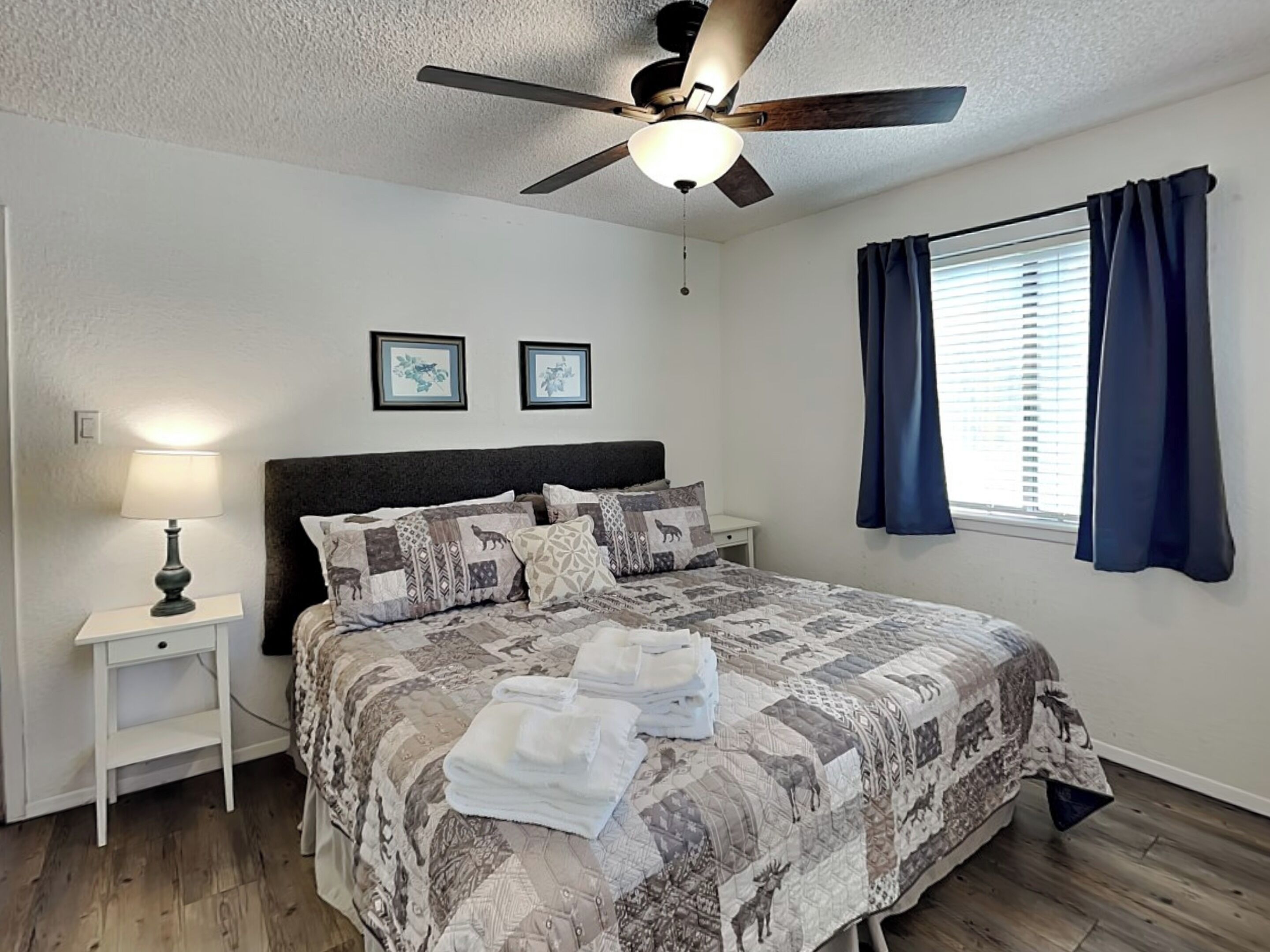 A bedroom with a bed, a nightstand, a ceiling fan, and a window with curtains.