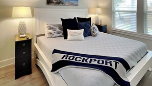 Een slaapkamer met een bed, twee nachtkastjes, een schilderij aan de muur en een raam met jaloezieën.