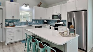 Een moderne keuken met witte kasten, een roestvrijstalen koelkast, een groot kookeiland met barkrukken en een blauwe tegelwand.