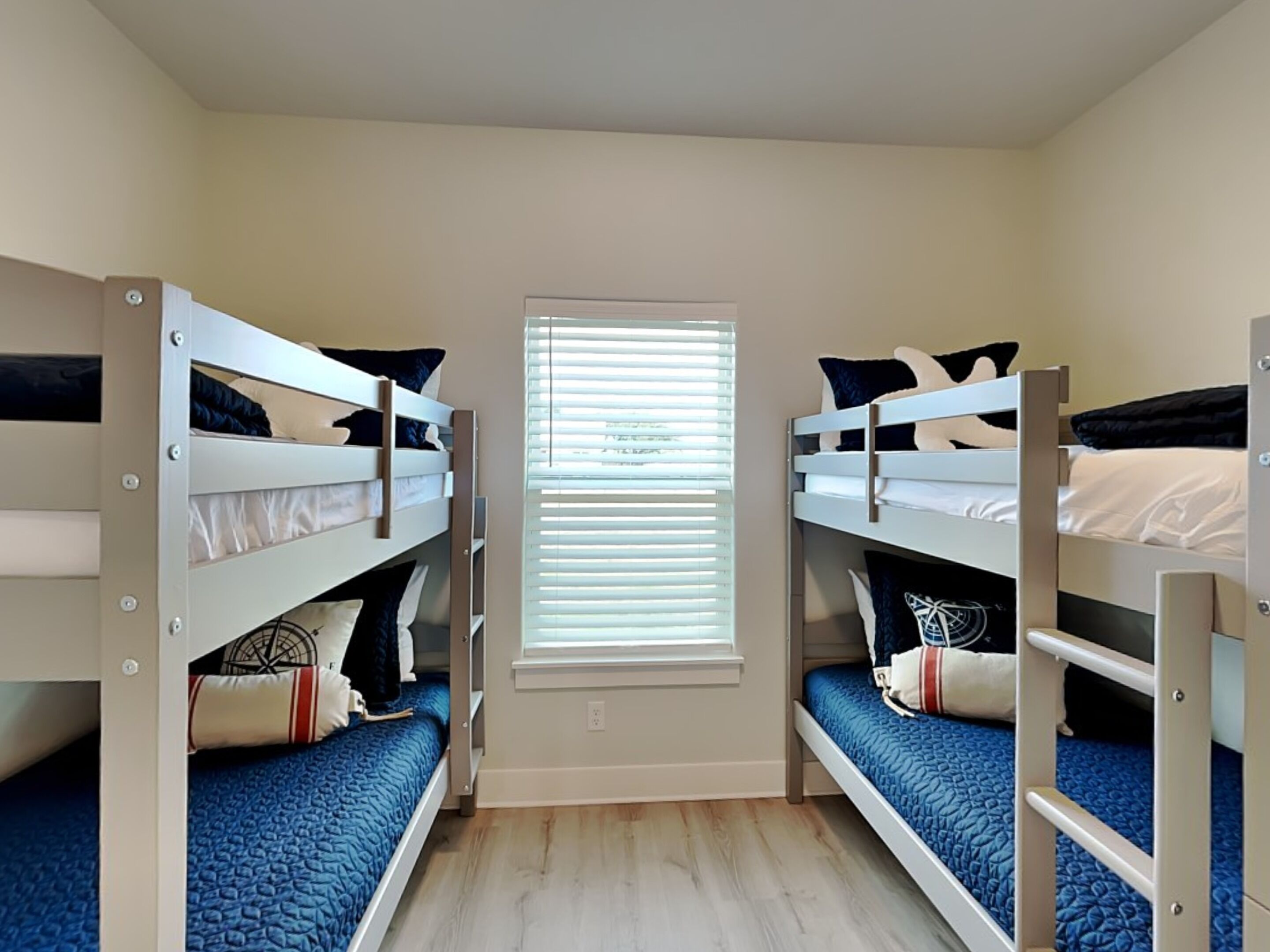 Een kamer met twee stapelbedden, een raam met zonwering, en een houten vloer.