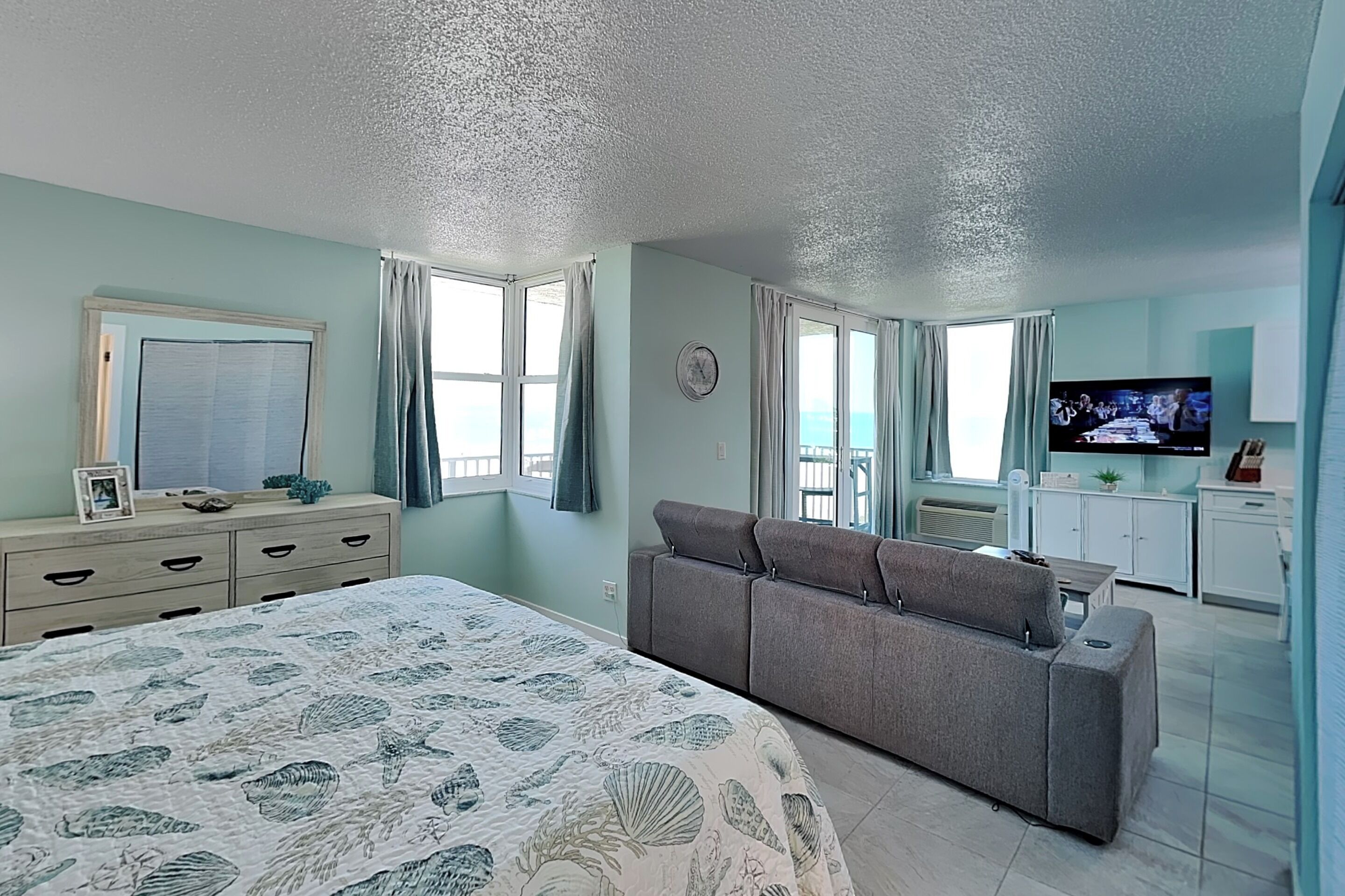 A bedroom with a bed, a sofa, a TV, and a kitchenette.