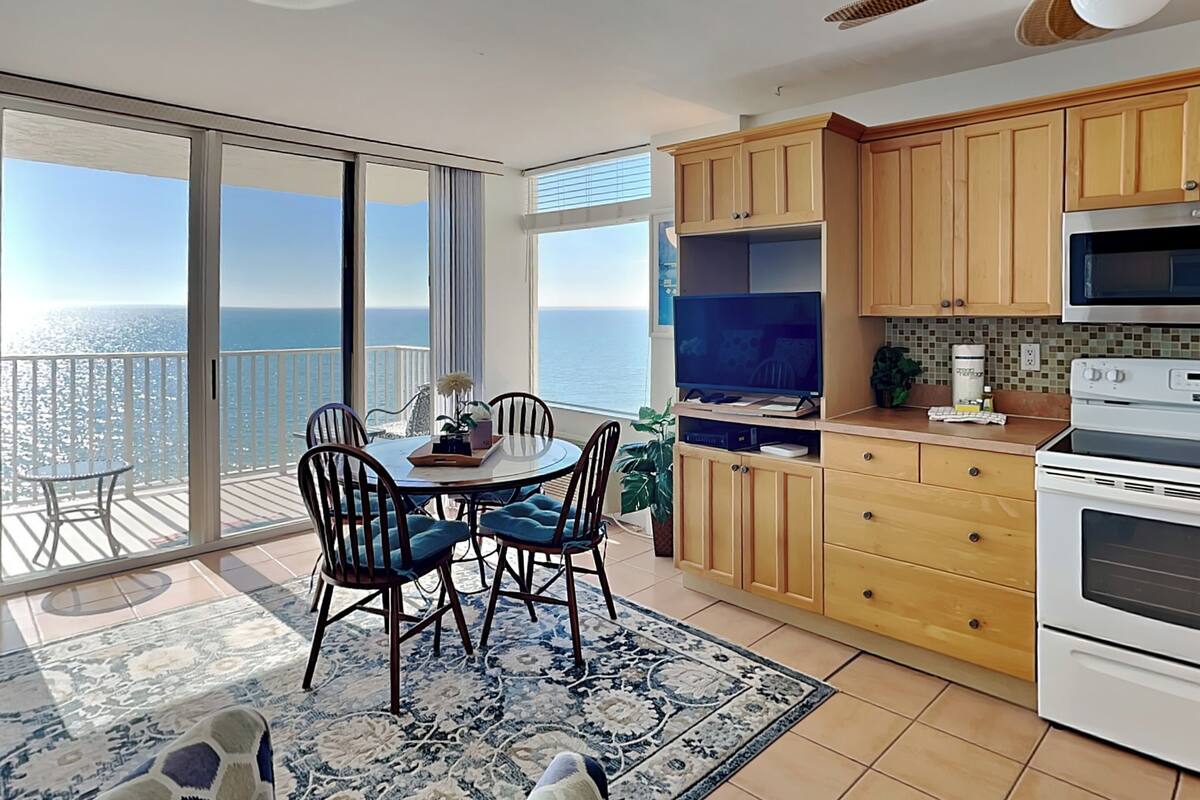 Une cuisine moderne avec des meubles en bois, un four encastré et une grande fenêtre donnant sur la mer.