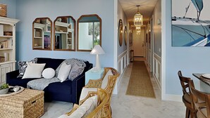 Ein Wohnzimmer mit einem dunkelblauen Sofa, Korbstühlen, einem Couchtisch und einem Essbereich mit Tisch und Stühlen.