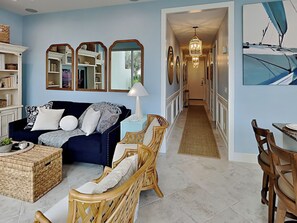 Ein Wohnzimmer mit einem dunkelblauen Sofa, Korbstühlen, einem Couchtisch und einem Essbereich mit Tisch und Stühlen.
