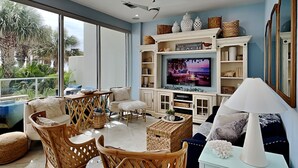 Ein geräumiges Wohnzimmer mit Rattanmöbeln, einem Fernseher und Blick auf Palmen.