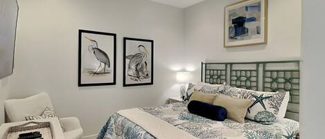 A bedroom with a bed, a desk, a chair, and artwork on the walls.
