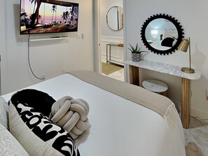 Une chambre à coucher moderne, avec un lit, une télévision, un miroir et une petite table sur laquelle est posée une plante.