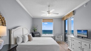 Une chambre à coucher comprenant un lit, une télévision, un ventilateur de plafond, une fenêtre donnant sur la mer et une commode.