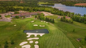 A golf course with a large pond, surrounded by trees and a building with multiple windows. - Bliss on the Bay (Birch Hill)