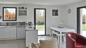 A modern kitchen with a dishwasher, a coffee maker, and a window overlooking a garden. There is a dining area with a white table and chairs, and a red chair in the foreground.