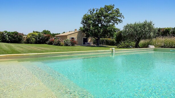 A clear swimming pool with a house and lush greenery in the background.