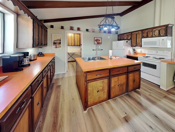 A kitchen with wooden cabinets, a central island, a microwave, a stove, and a coffee maker. - Our Perky Place by Ruidoso Vacation Rentals (Ruidoso)