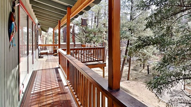 Eine überdachte Terrasse im Freien mit Holzgeländern, einer Bank und Blick auf einen bewaldeten Bereich.