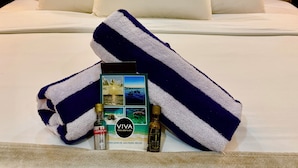 Hotelkamer met een bed, witte kussens, een gestreept handdoek, een fles drank en een brochure op het bed.