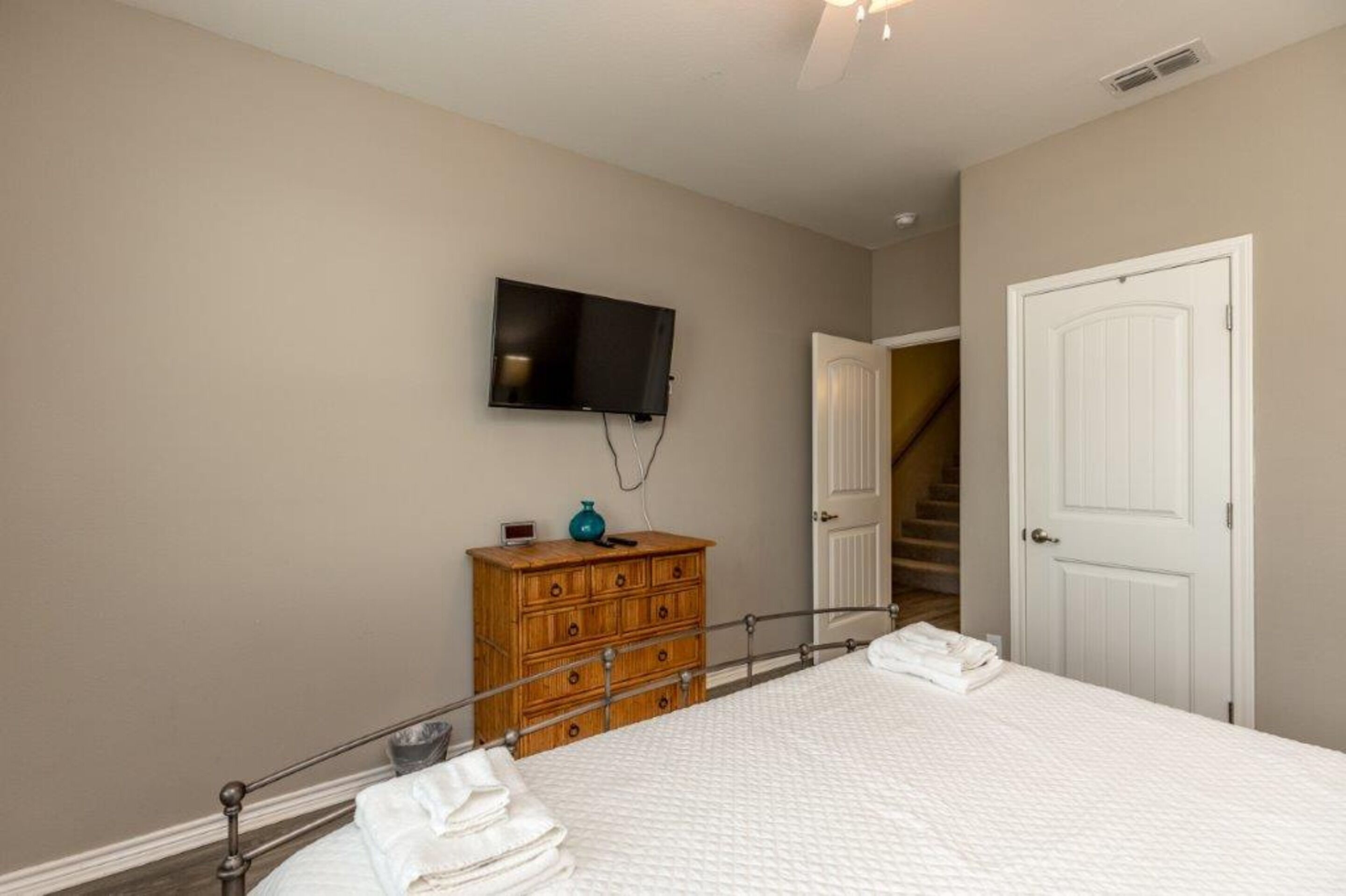 A bedroom with a bed, a wooden dresser, a television mounted on the wall, and a white door.